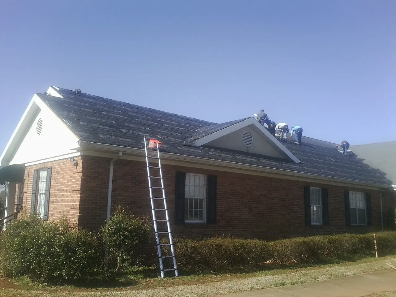 Crew tearing shingles off a brick ranch roof with a ladder set — Emergency Roof Repair work by our crew in Mt Baldy