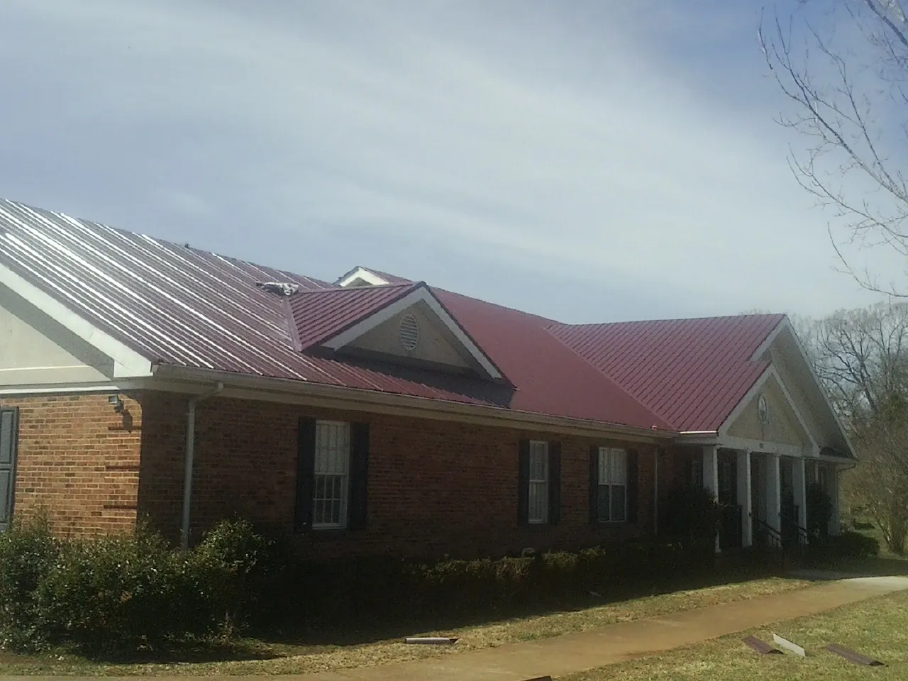 Red metal roof with gabled entries on a long brick building, from a Hail Damage Roof Repair job in Mt Baldy