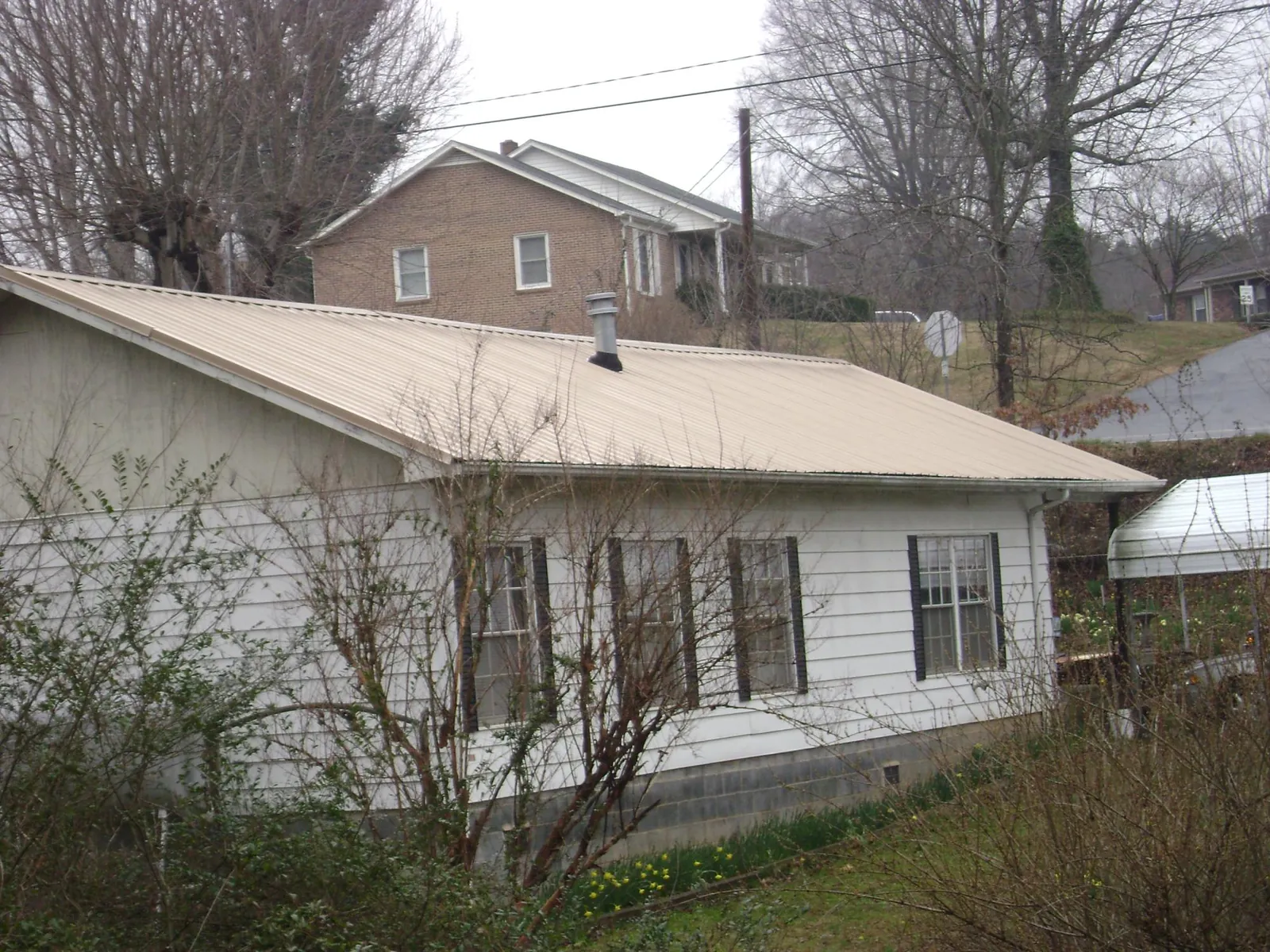 Tan metal roof on a white sided house set into a hillside — Commercial Roofing by Roofing Brothers in Mt Baldy
